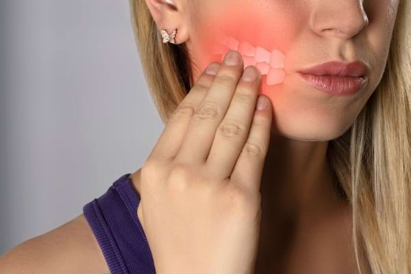 Femme se tenant la joue avec douleur dentaire visible.