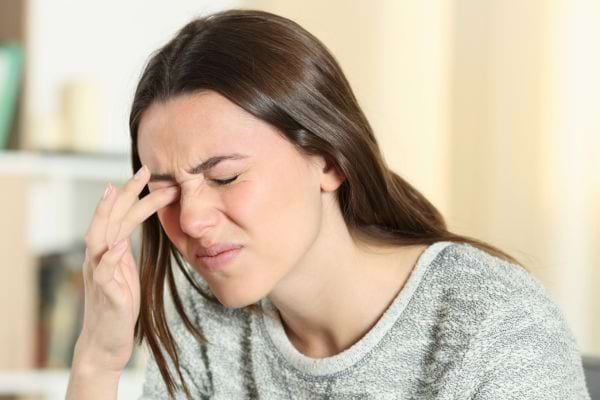 Une femme grimace en se frottant l’œil douloureux.