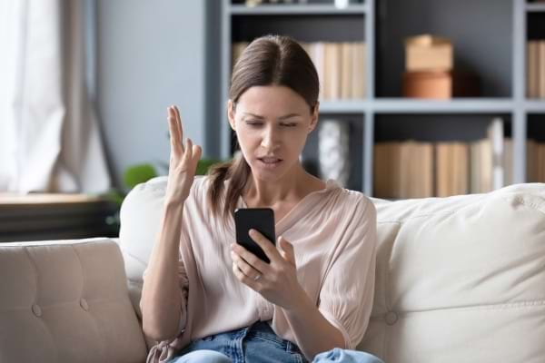 Une femme contrariée regarde son téléphone sur un canapé.