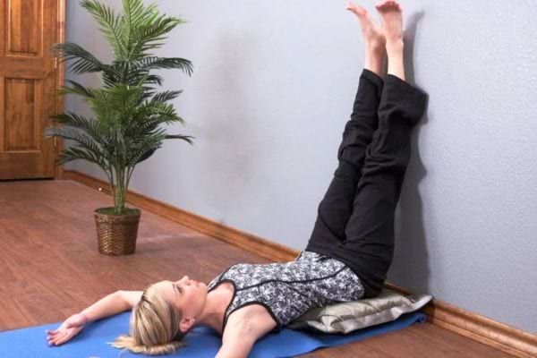 Femme allongée sur un tapis jambes relevées contre le mur.