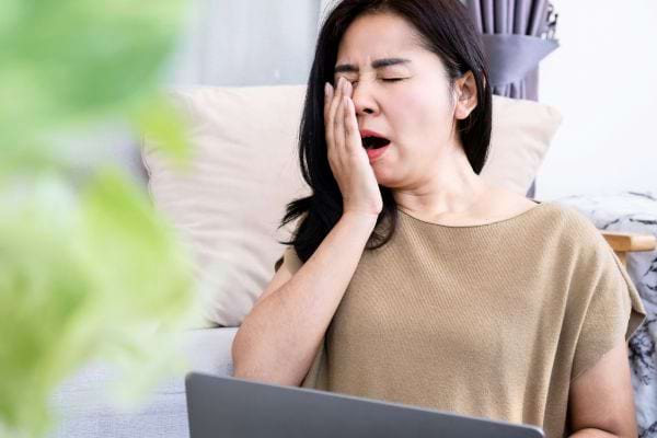Une femme assise baille devant son ordinateur portable.