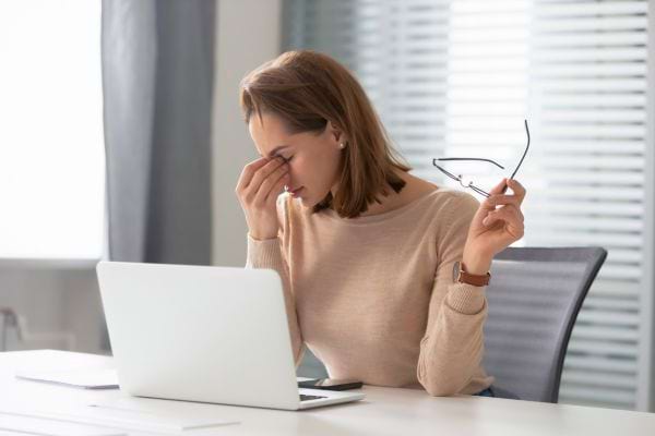 Une femme fatiguée se masse les yeux devant son ordinateur portable.