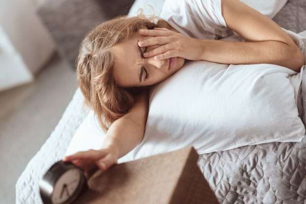 Une femme fatiguée s’étire au réveil en éteignant son réveil sur la table de chevet.