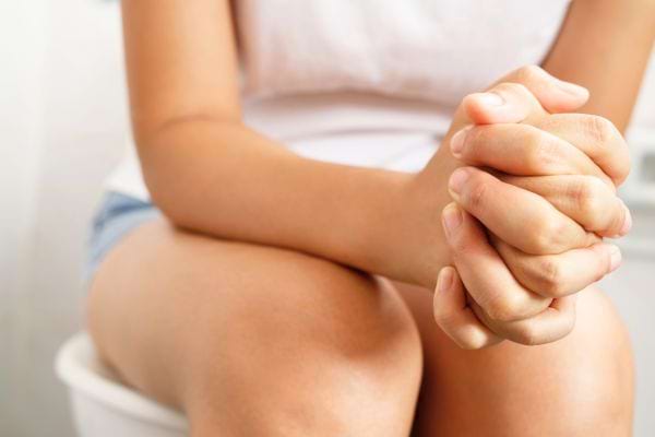 Une femme assise sur les toilettes joint ses mains en signe d’inconfort.