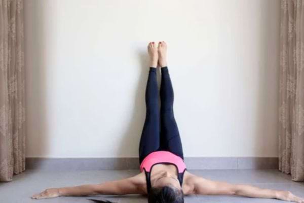 Femme allongée au sol jambes contre le mur.