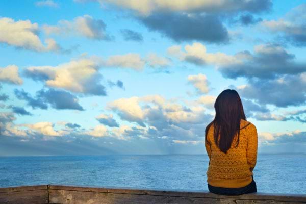  Une femme assise regarde la mer et l’horizon au loin.