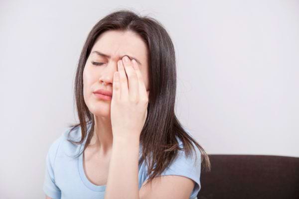 Une femme souffre d’une forte migraine en tenant son œil fermé.