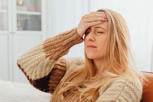 Une femme assise sur un canapé pose sa main sur son front avec douleur.