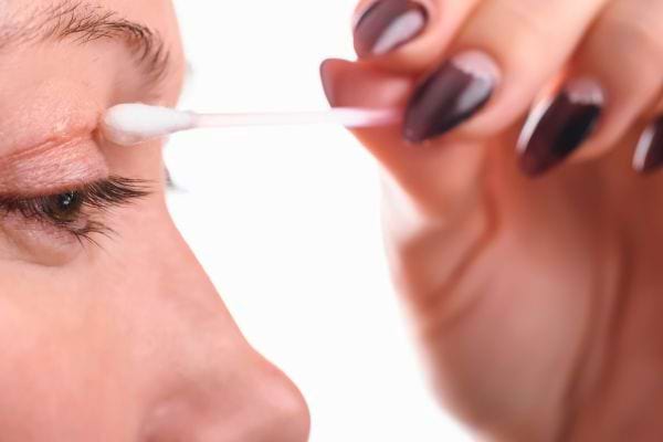 Une femme nettoie doucement sa paupière avec un coton-tige.