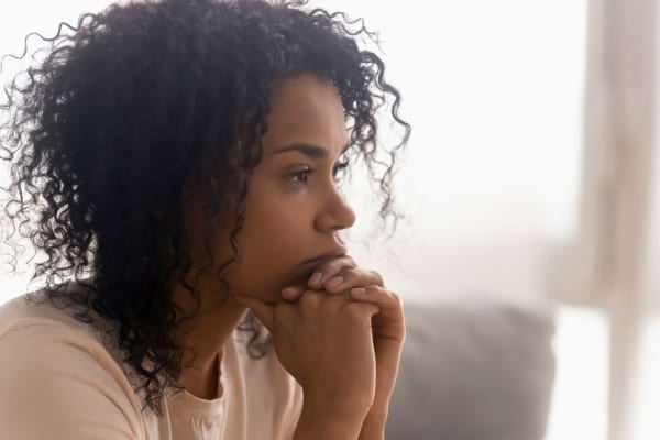 Femme pensive assise, regardant au loin, l'air préoccupé.