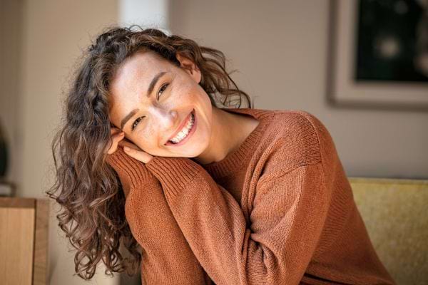 Femme souriante en pull brun appuyée sur ses mains.