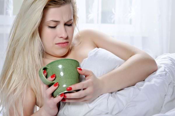 Femme allongée tenant une tasse avec une grimace de dégoût.