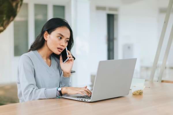 Une femme parle au téléphone tout en travaillant sur son ordinateur portable à l’extérieur.