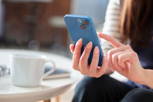 Femme tenant un smartphone bleu et tapotant l’écran.