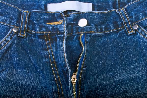 Jean bleu avec fermeture éclair ouverte et bouton métallique visible.