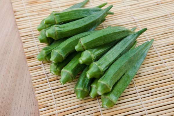 Des gombos verts bien alignés reposent sur un tapis en bambou.