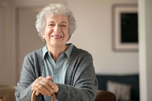 Une grand-mère souriante aux cheveux gris assise avec un gilet gris.