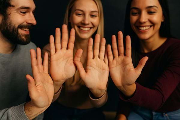 Trois personnes souriantes montrent leurs paumes ouvertes face à la caméra.