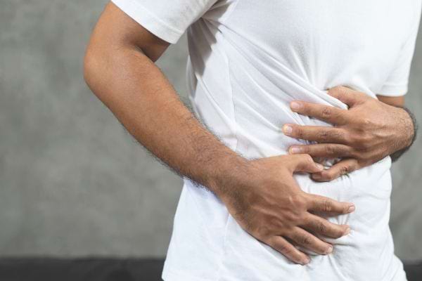 Un homme en t-shirt blanc se tient le ventre douloureux.