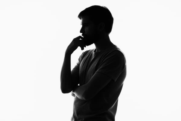 Un homme est en pleine réflexion, silhouette noire sur fond blanc.