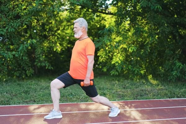 Un homme âgé fait une fente avec des haltères en extérieur.