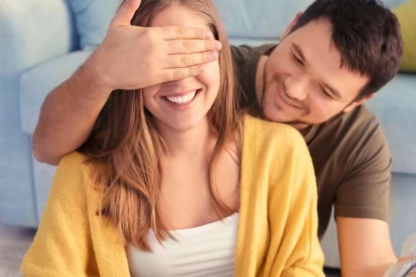 Homme couvrant les yeux d’une femme souriante.