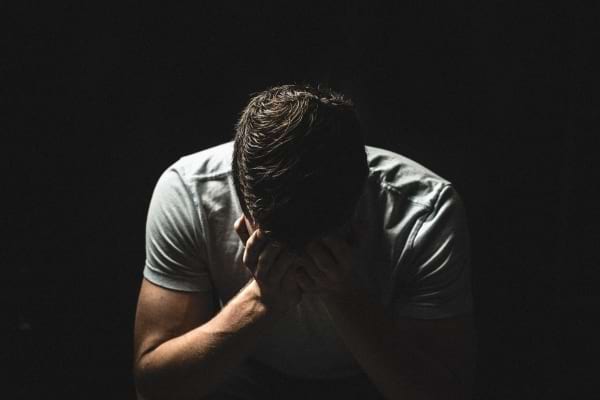 Homme assis dans le noir, tête entre les mains.