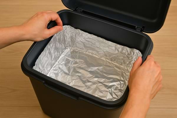 Mains ajustant le papier aluminium dans la poubelle.