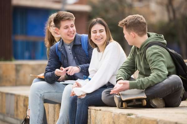 Des adolescents assis discutent et rient entre amis dehors, sur des marches en pierre.