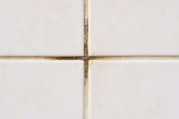 Joint de carrelage blanc encrassé avec des traces noires visibles.