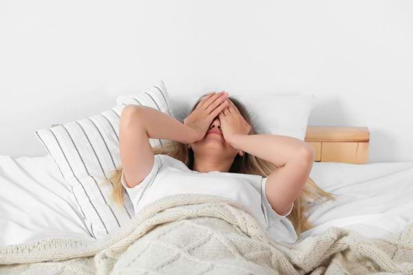Une femme allongée dans son lit se cache le visage fatiguée.