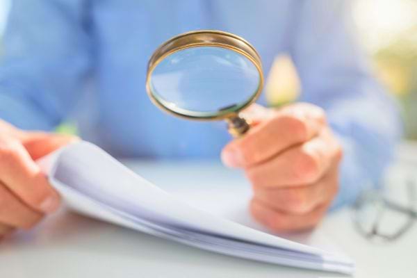 Personne tenant une loupe au-dessus d’un document.