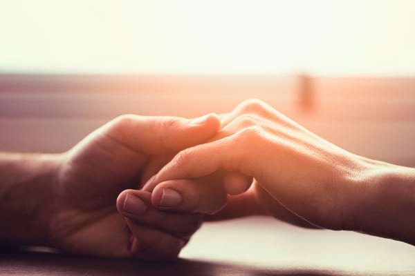 Deux mains s’effleurent tendrement, geste discret de connexion affective.