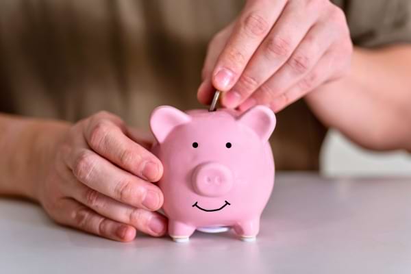 Main insérant une pièce dans une tirelire rose.