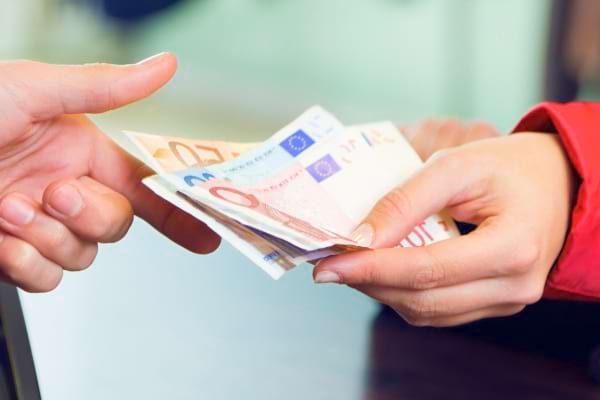 Main tendant plusieurs billets d’euros à une autre personne, lors d’un paiement.