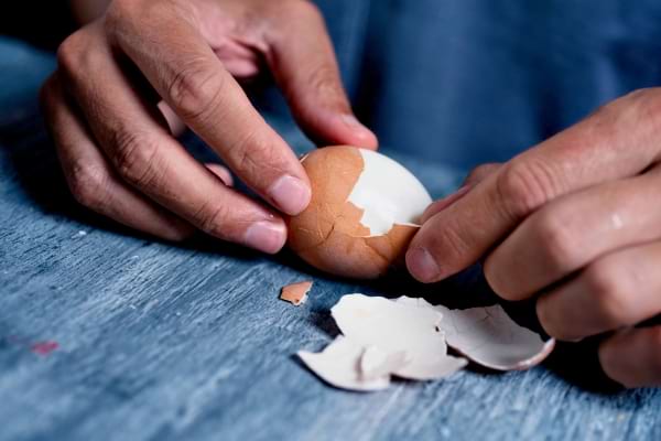 Mains épluchant un œuf dur en retirant la coquille brune.