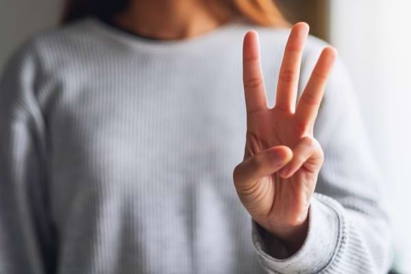 Main d’une femme montrant trois doigts. 