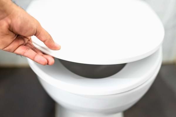 Main abaissant le couvercle des toilettes.