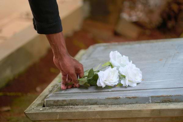 Un homme dépose des fleurs blanches sur une tombe.