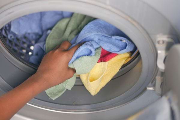 Une main insère des serviettes colorées dans le tambour de la machine à laver.