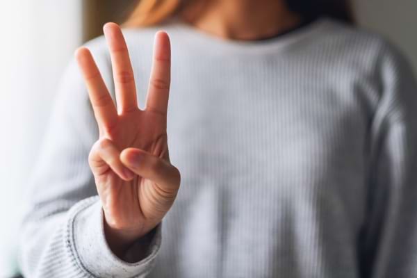 Une femme lève trois doigts pour illustrer un chiffre.