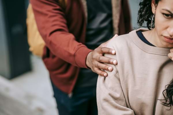 Un homme pose sa main sur l’épaule d’une femme triste, elle reste distante et fermée.