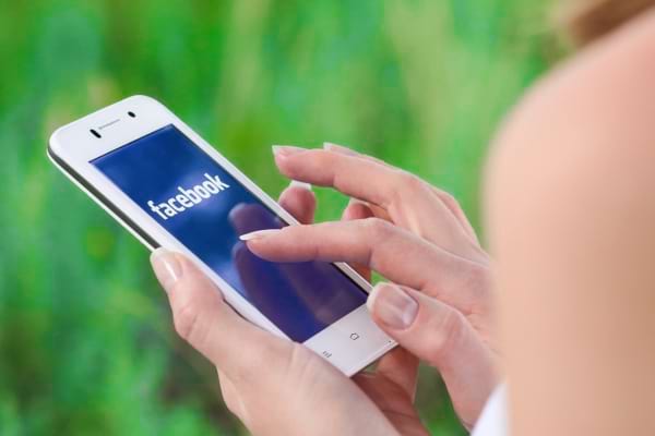 Main tenant un smartphone affichant l’application Facebook.