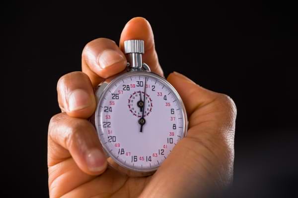 Une main tient un chronomètre argenté sur fond noir.