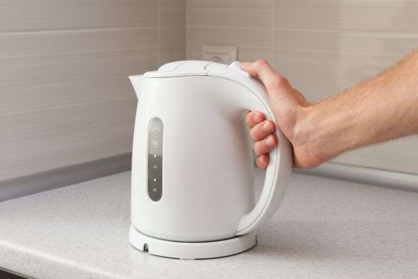 Main tenant une bouilloire électrique blanche posée sur un plan de travail.
