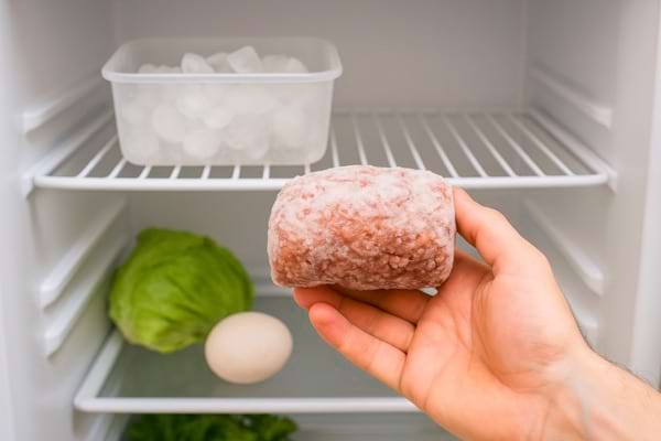 Main tenant un morceau de viande congelée dans un réfrigérateur.