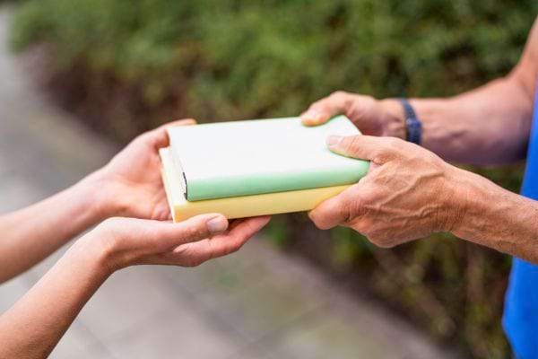 Deux personnes échangent un cadeau emballé, l’une tendant le paquet et l’autre le recevant.