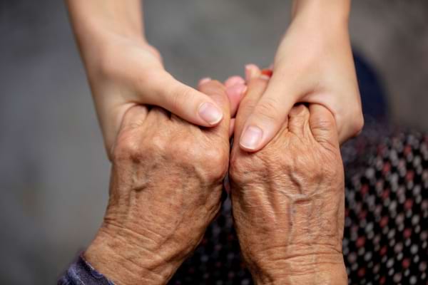 Deux mains tiennent celles d’une personne âgée en signe de soutien.