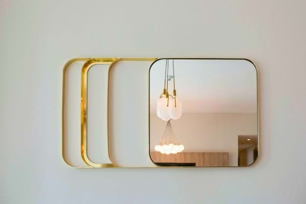 Miroir mural doré reflétant un luminaire.