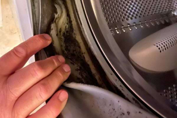 Main soulevant un joint de machine à laver couvert de saleté noire.